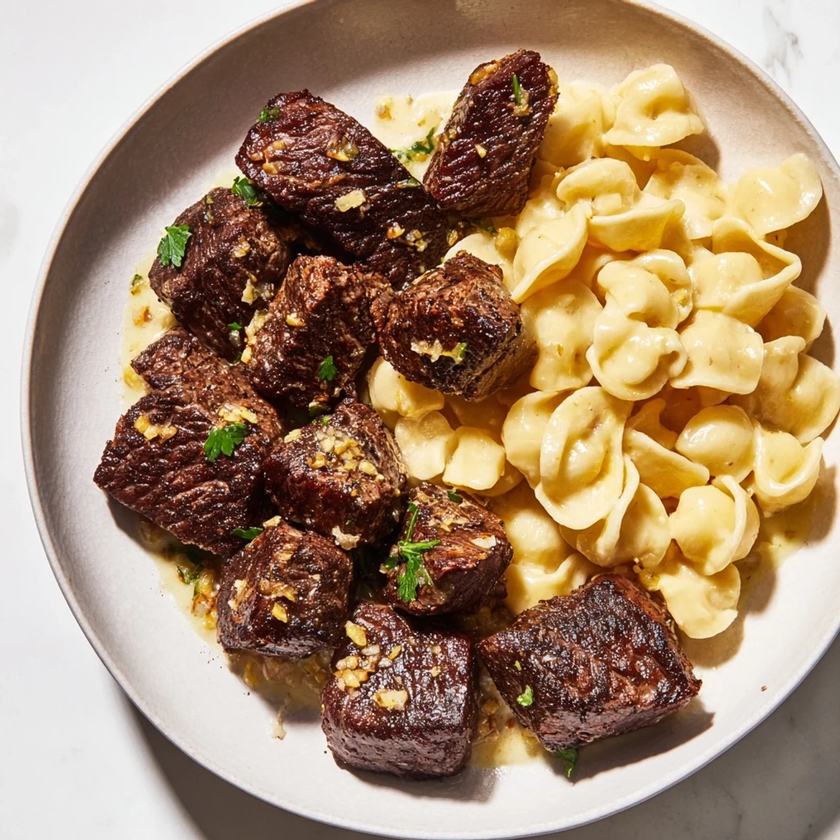 A close-up of savory garlic butter steak bites and cheesy shells, ready for a delicious dinner.
