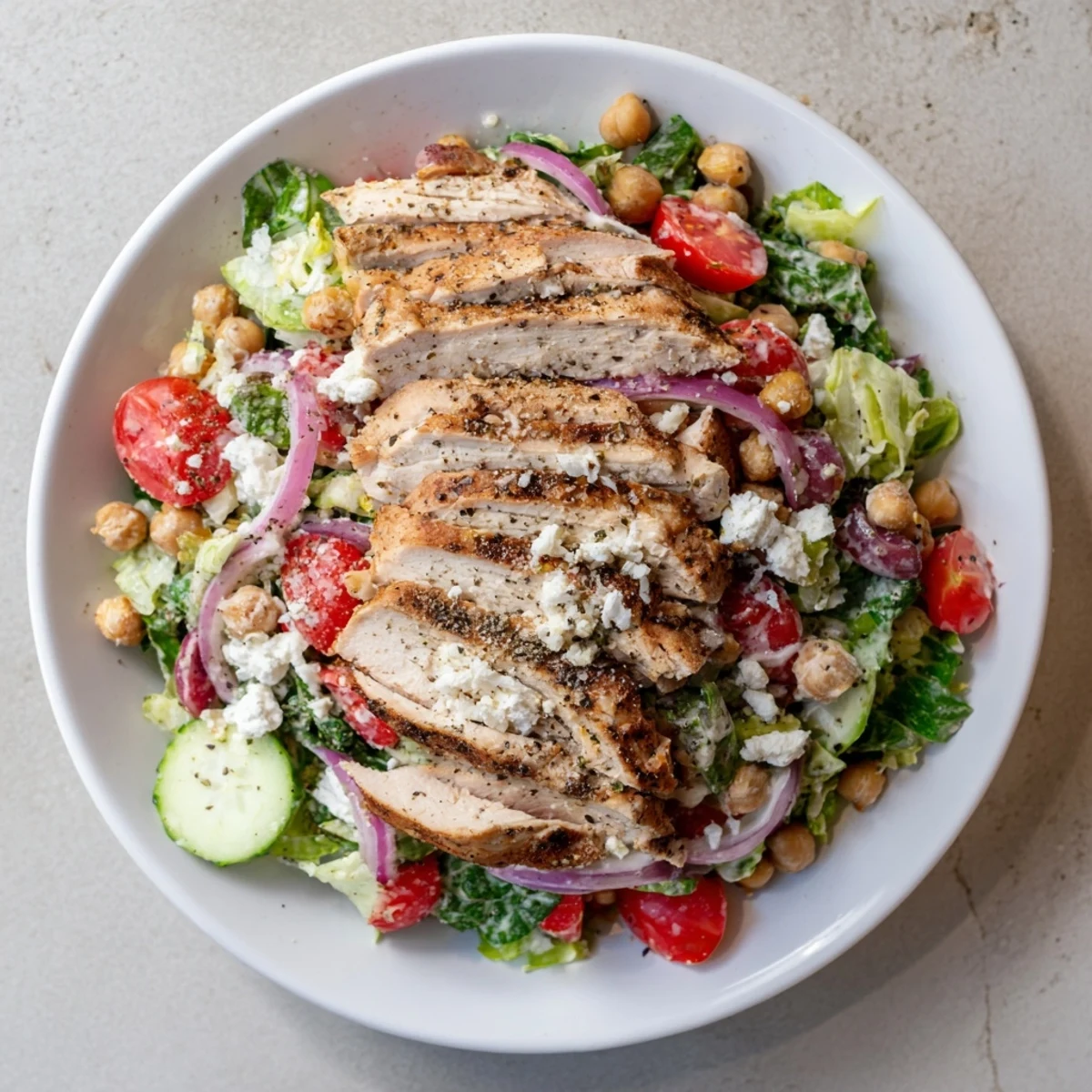 Grilled chicken atop a colorful Chicken Caesar Pasta-less Bowl with creamy dressing and parmesan.