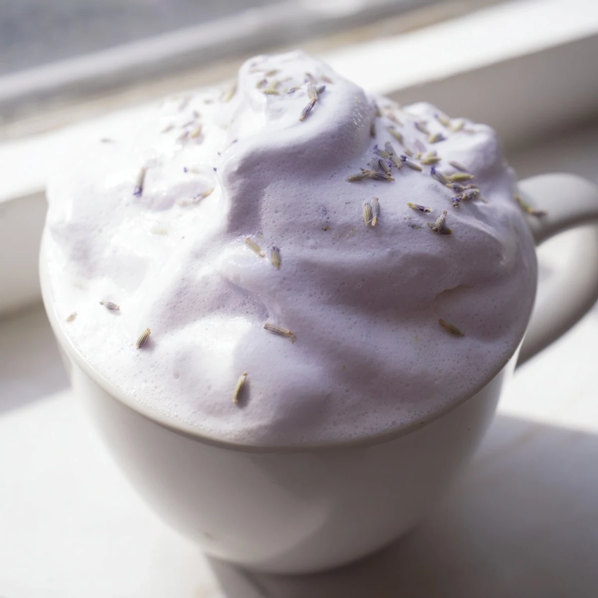 Creamy espresso and lavender syrup topped with fluffy whipped foam in a glass mug, perfect for a relaxing afternoon treat.  