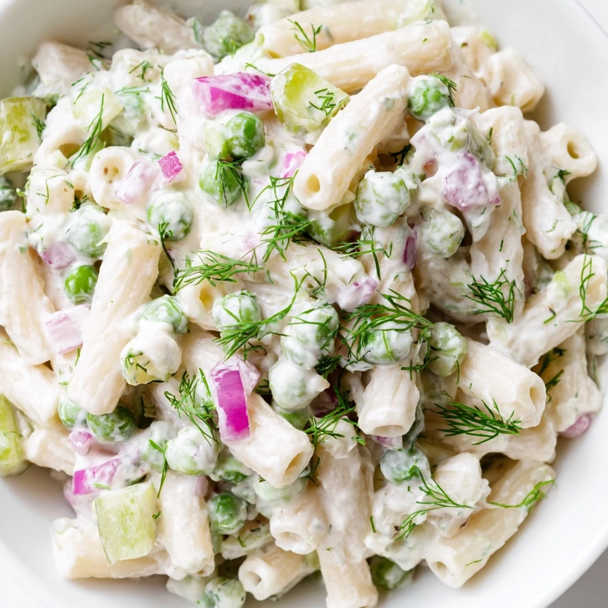 A vibrant bowl of creamy dill pickle pasta salad with ditalini, green peas, and fresh dill garnish.  