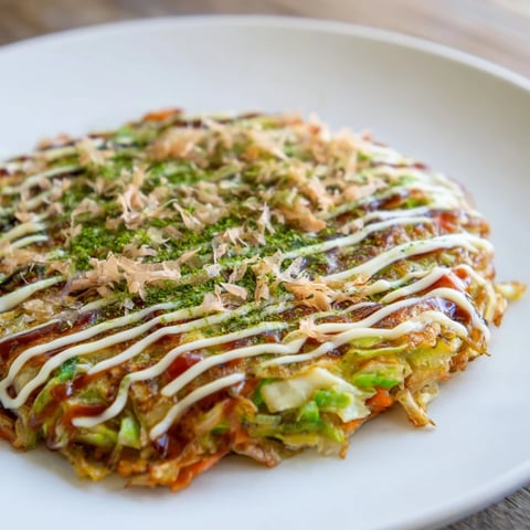 Golden okonomiyaki pancakes, perfectly cooked and topped with savory okonomiyaki sauce and dancing bonito flakes.