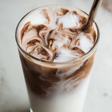 A tall glass of homemade Milo Ice Latte Hack with ice cubes and a straw, showcasing its creamy chocolatey layers.