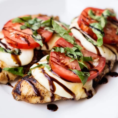 A close-up of Caprese Chicken Skillet with melted mozzarella, juicy tomatoes, and fresh basil on a rustic skillet.