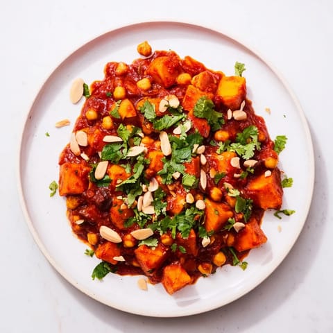 A close-up of a fragrant Moroccan Chickpea & Sweet Potato Tagine, served with fresh cilantro and lemon wedges.