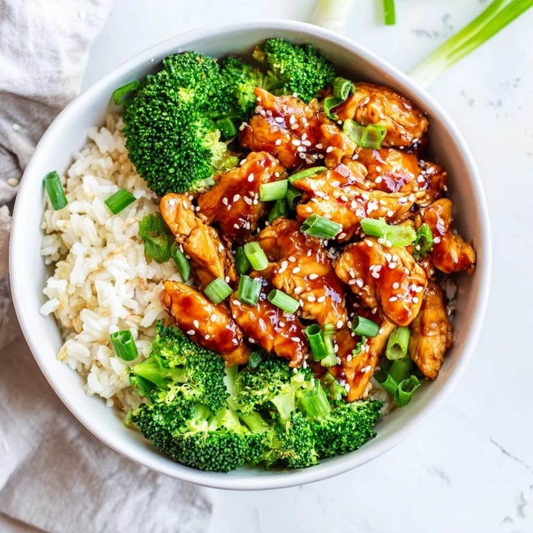 In a softly lit kitchen, the Sweet Chili Chicken Bowl garnished with sesame seeds and green onions sits ready to enjoy.