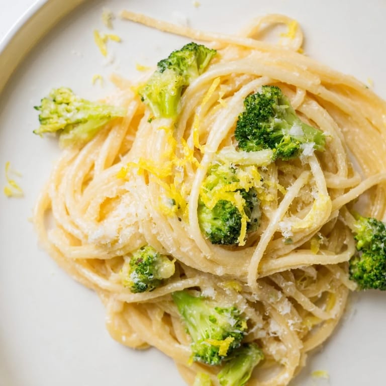 Bright one-pot lemon broccoli pasta glistens with olive oil and fresh herbs, steaming beside a crisp white wine on a table.
