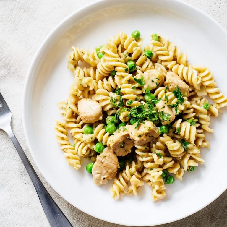 A close-up of saucy chicken and pea pasta, steam rising, showing the creamy texture and golden Parmesan topping.